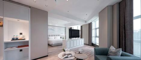 A modern hotel room with a large bed, a seating area with a sofa and coffee table, a TV, and a large window offering a city view.