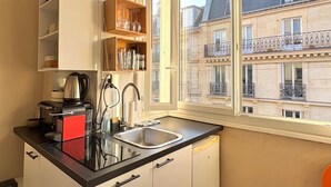 A kitchen with a window, a coffee maker, a sink, and a cabinet with glassware. - Studio Quartier Latin & Seine (Paris)