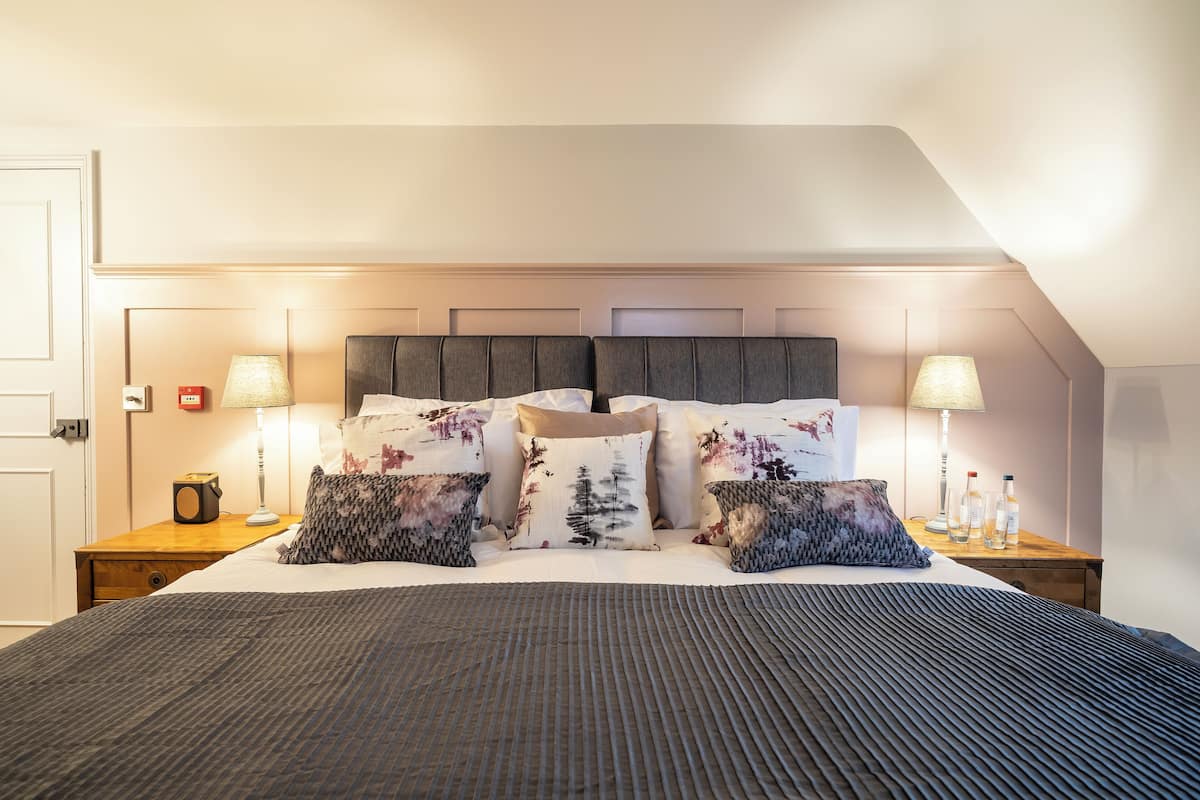 Una cama bien hecha con una colcha estampada, dos mesitas de noche con lámparas y un cabecero con diseño geométrico.