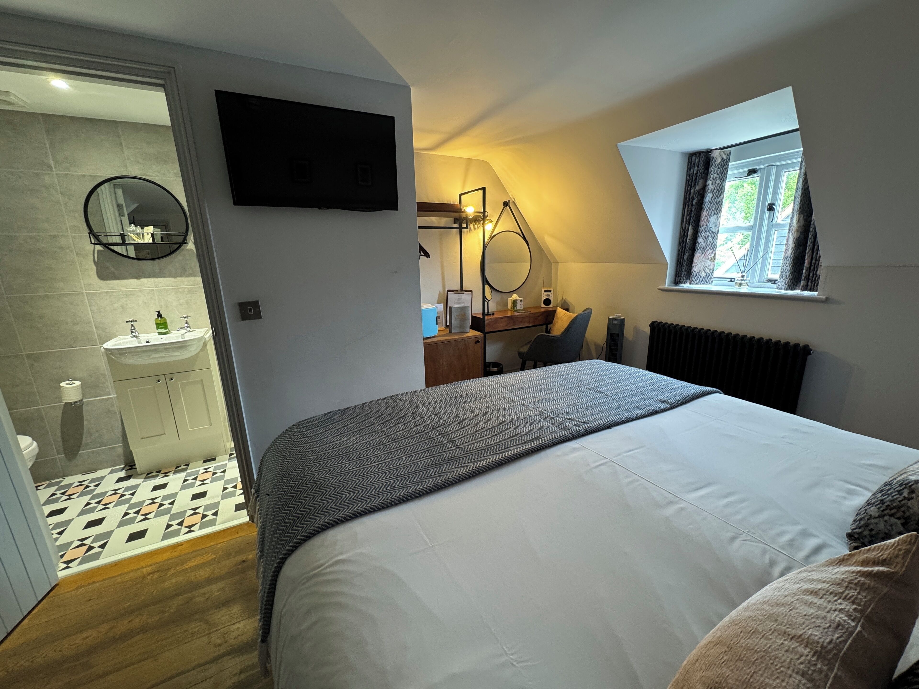 Une chambre avec un grand lit, un bureau avec une chaise, un miroir et une fenêtre.