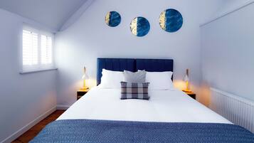A neatly arranged bedroom with a large bed, two bedside lamps, a window with blinds, and three wall art pieces.