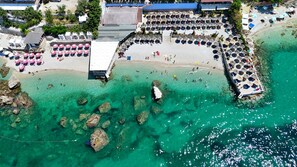 An aerial view of a beach with clear turquoise water, rocky outcrops, and a pavilion with umbrellas. - La Terrazza Azzurra (Vlore)