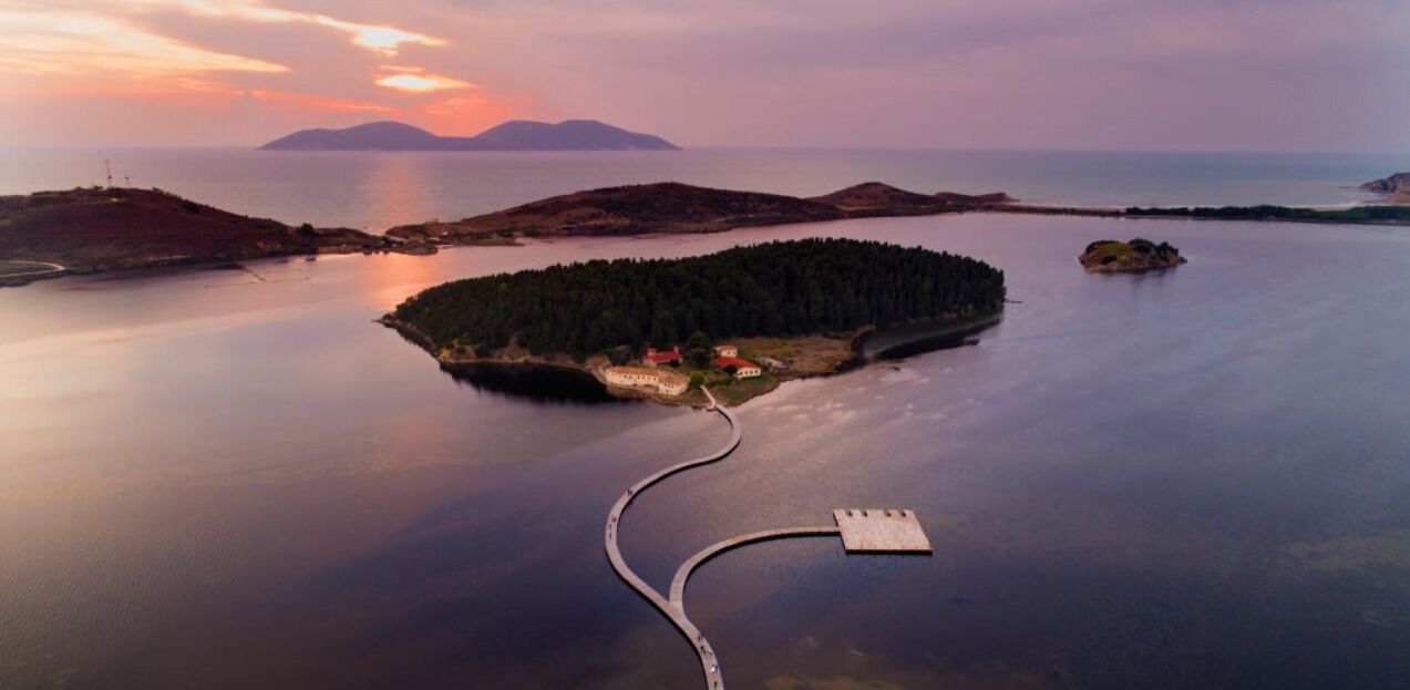 An aerial view of a coastal island with a dock leading to a small island with buildings.