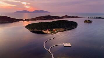 An aerial view of a coastal island with a dock leading to a small island with buildings.