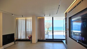 A modern living room with a large TV, a fireplace, and a view of the sea. - La Terrazza Azzurra (Vlore)