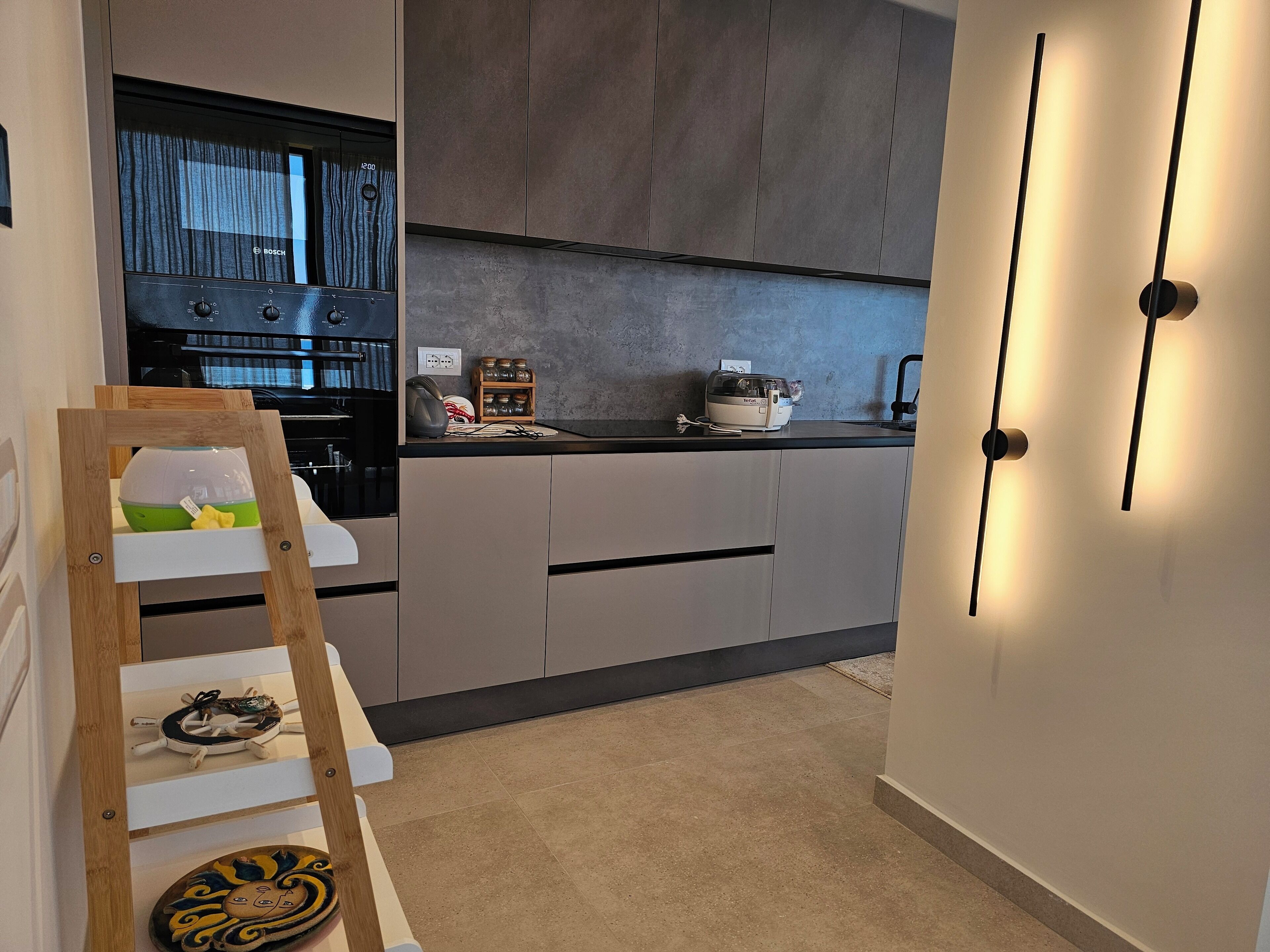 Cozinha moderna com armários cinza, forno Bosch, torradeira e escada de madeira.