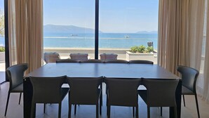 A dining area with a large table and chairs, a view of the sea with ships, and a balcony with plants. - La Terrazza Azzurra (Vlore)