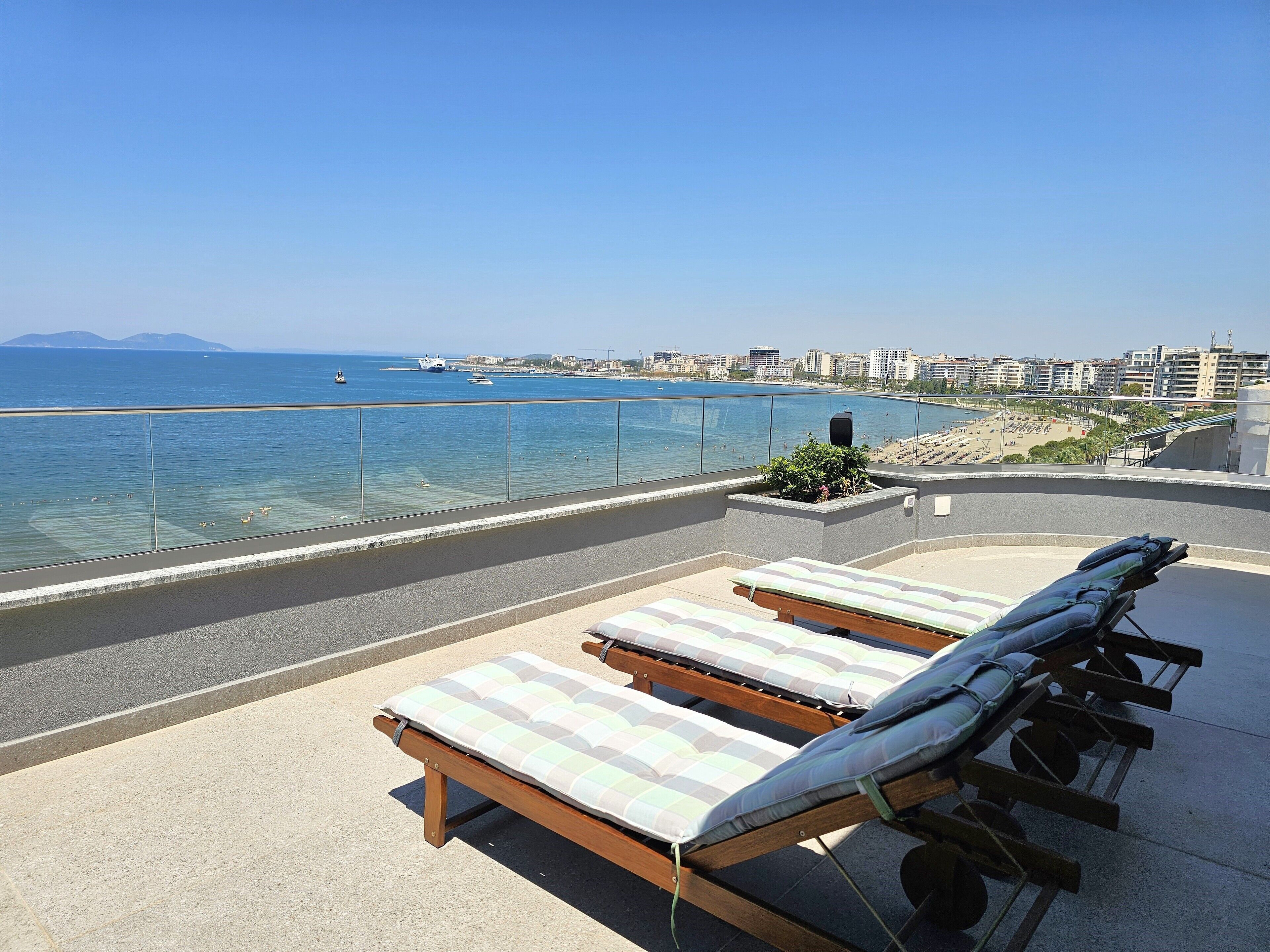 Une terrasse sur le toit, dotée de chaises longues et offrant une vue sur la mer et le paysage urbain.