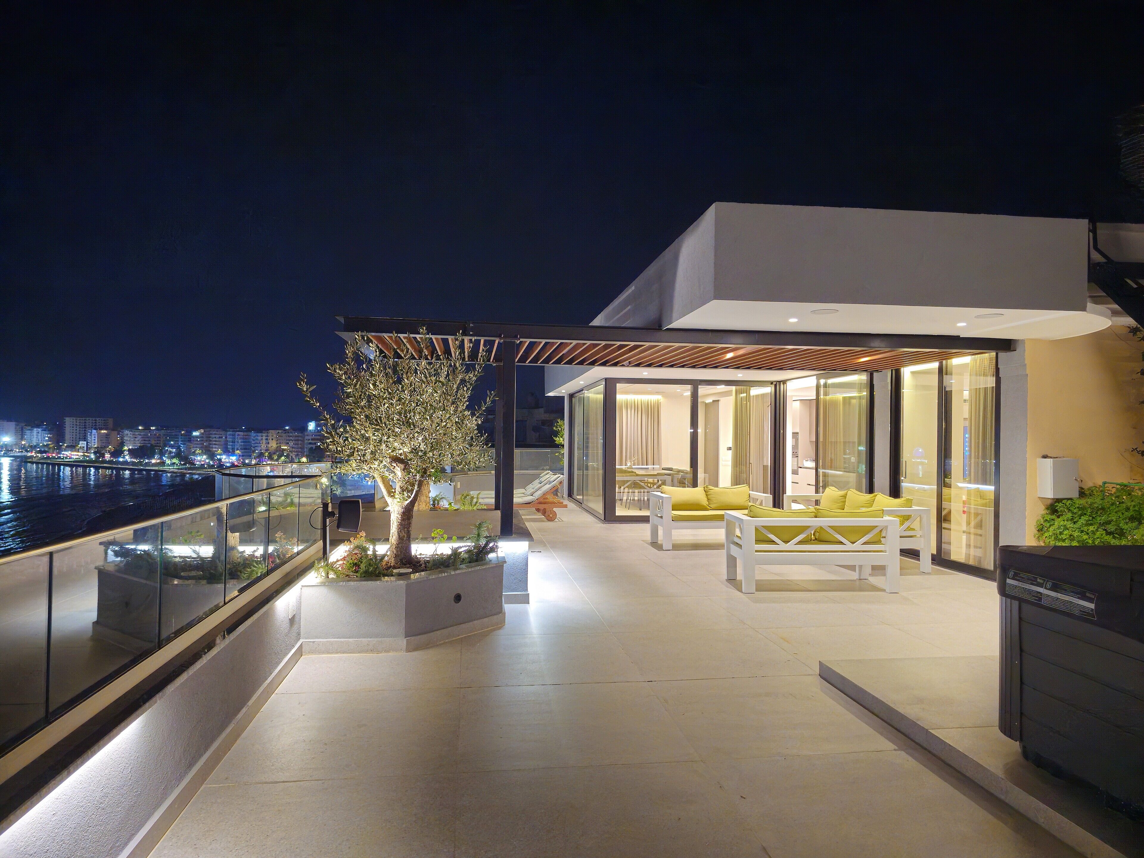 A modern outdoor terrace with a glass railing, a tree, and yellow seating.