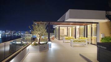 A modern outdoor terrace with a glass railing, a tree, and yellow seating.
