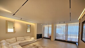 A modern living room with a sectional sofa, a flat-screen TV, and large windows with sheer curtains. - La Terrazza Azzurra (Vlore)