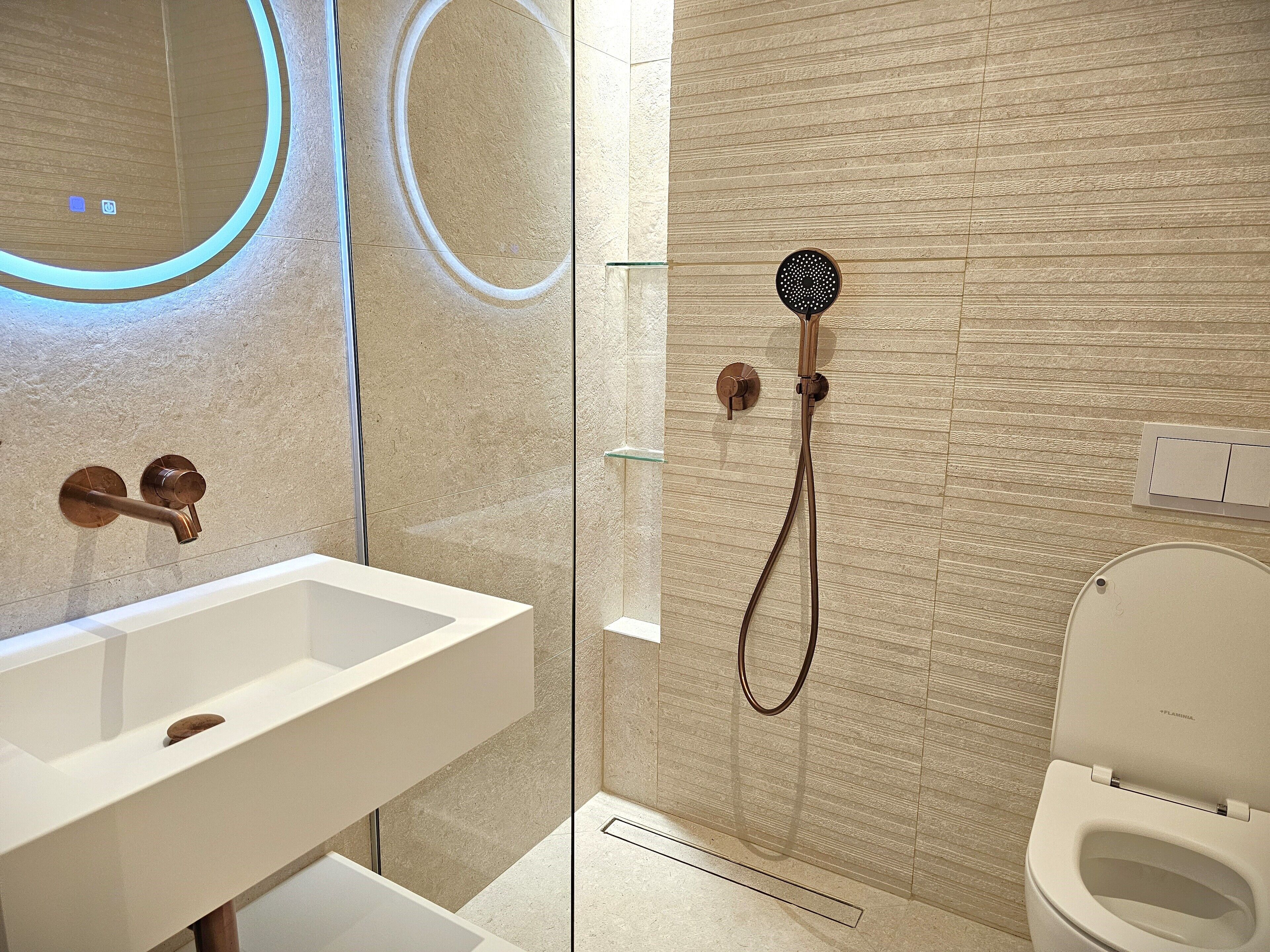 A modern bathroom with a white sink, a glass-enclosed shower, and a toilet.
