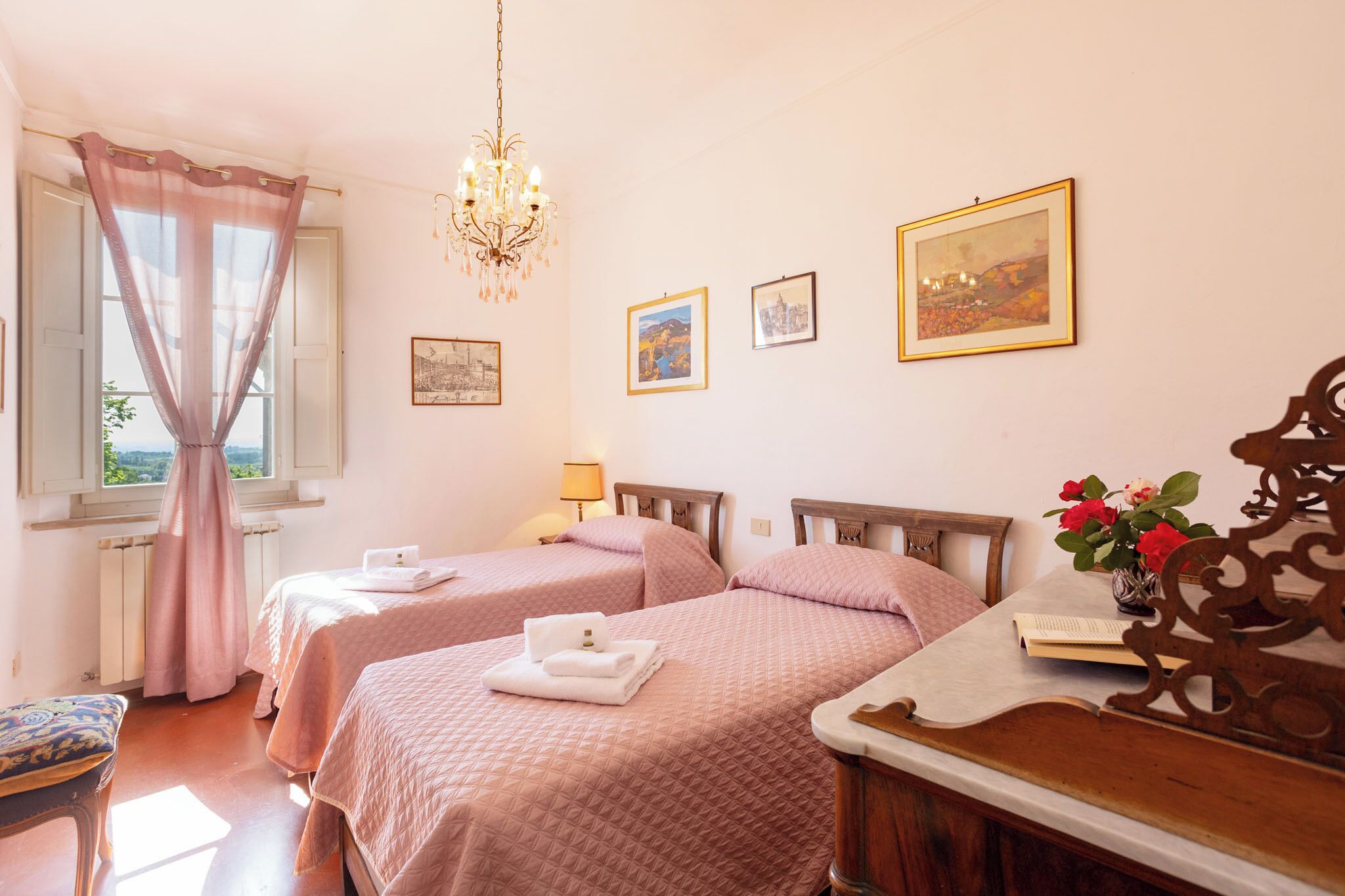 Une chambre d’hôtel avec deux lits, un lustre, des tableaux encadrés au mur et une vue sur la verdure.