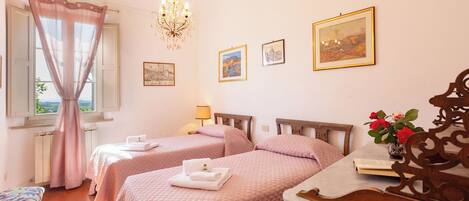 Une chambre d’hôtel avec deux lits, un lustre, des tableaux encadrés au mur et une vue sur la verdure.