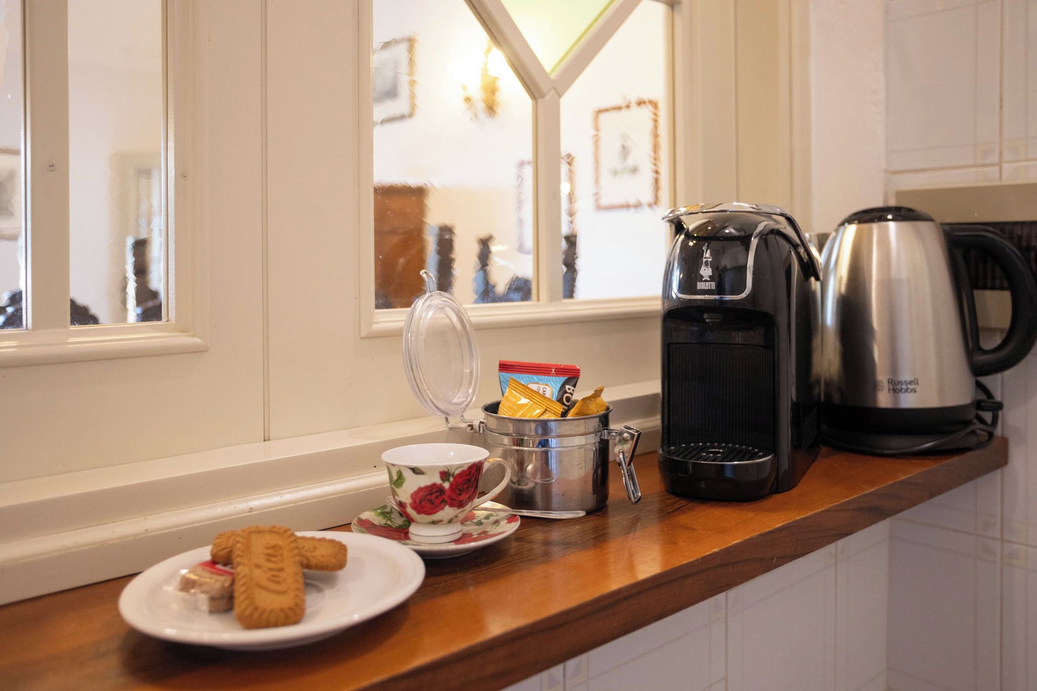 A kitchen counter with a coffee maker, a kettle, a mug, and a plate with cookies.
