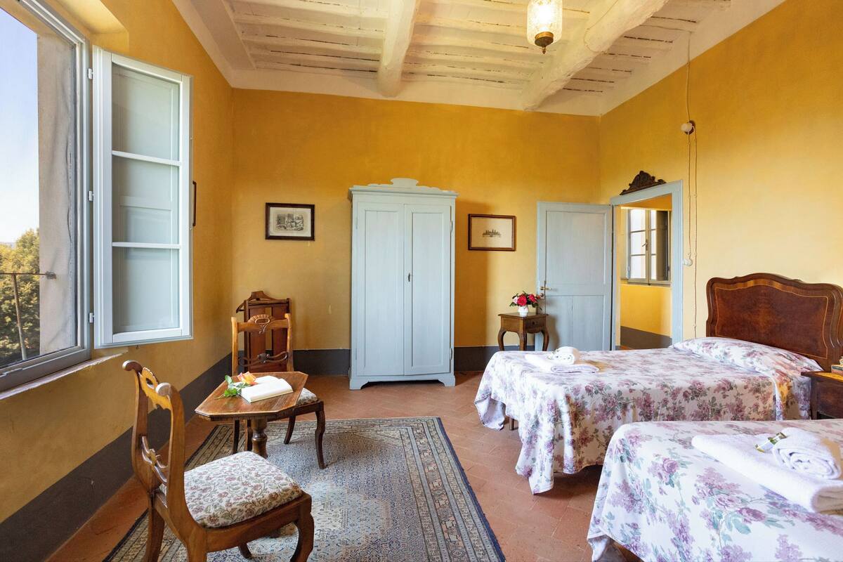 A room with two beds, a wooden chair, a table, a cabinet, and a window.