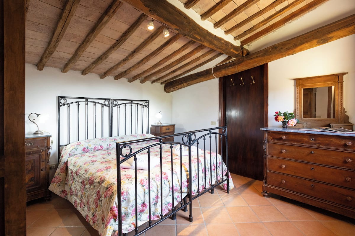 A bedroom with a bed, wooden dresser, and a mirror.