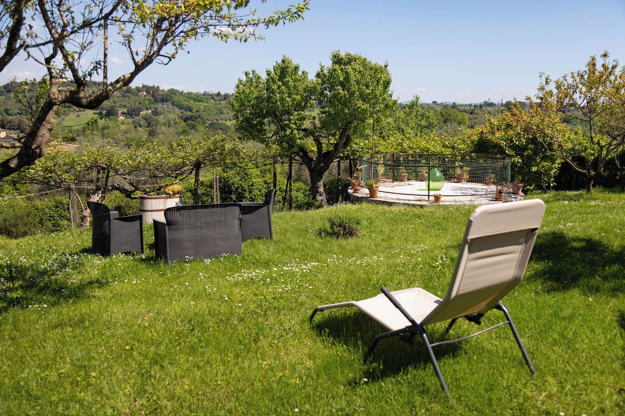 A grassy outdoor area with a chair and a table, surrounded by potted plants and a view of a distant landscape.