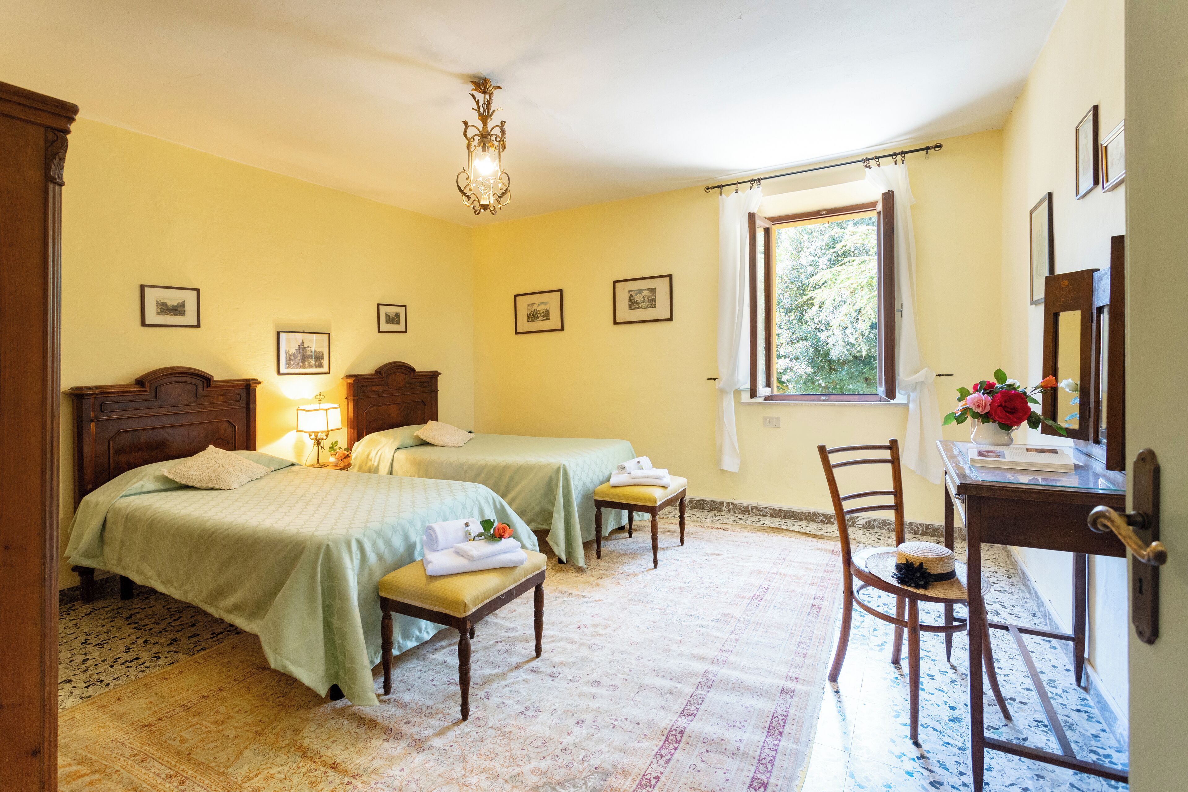 Habitación de hotel con dos camas, un escritorio, una silla, una ventana con vistas y una araña.