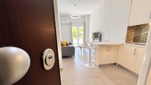 A modern kitchen with white cabinets, a grey sofa, and a dining area with a table and chairs. - Downtown Bliss – Piraeus Street by ΜΡS (Athina)