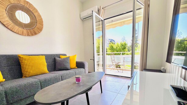 A modern living room with a grey sofa, yellow cushions, a round wall decoration, and a glass door leading to an outdoor area. - Downtown Bliss – Piraeus Street by ΜΡS (Athina)
