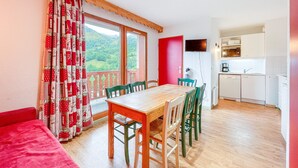 A dining area with a wooden table and chairs, a red wall, and a kitchen in the background.