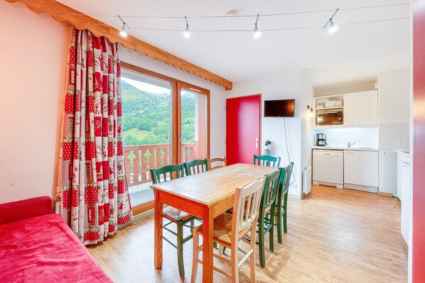 A dining area with a wooden table and chairs, a red wall, and a kitchen in the background.