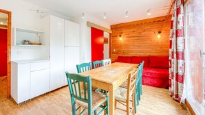 A dining area with a wooden table and chairs, a red sofa, and a kitchen area with white cabinets.