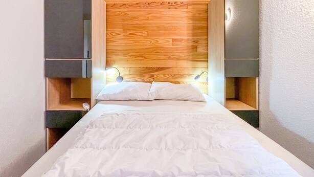 A narrow room with a bed, wooden headboard, and built-in storage cabinets.