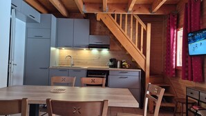 A compact kitchen with grey cabinets, a wooden dining table, and a staircase leading to a loft area.