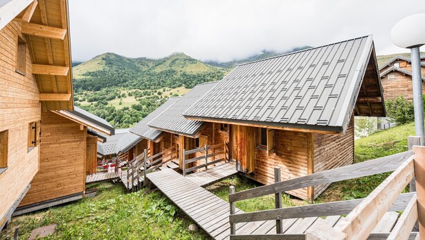 A wooden cabin with a sloped roof, wooden deck, and a view of a green valley.