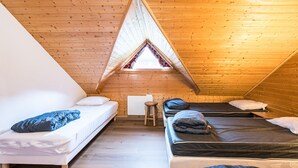 A triangular attic bedroom with wooden walls, two beds, a small stool, and a window.