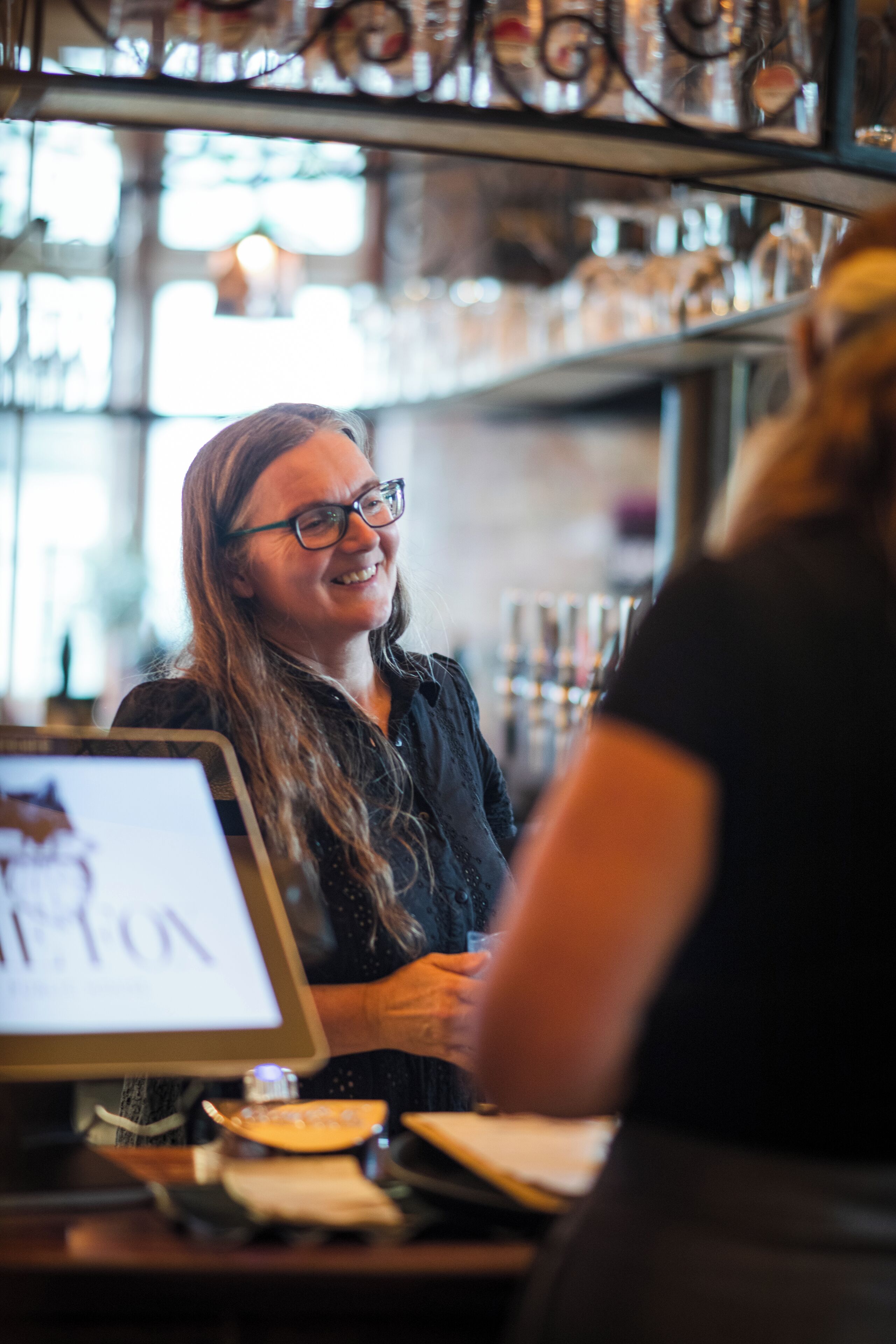 Eine Bar mit Computermonitor, der eine Speisekarte zeigt, einer Registrierkasse und einer Bar.