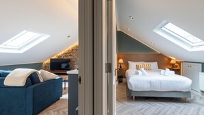 A modern bedroom with a skylight, a bed, a sofa, and a television.