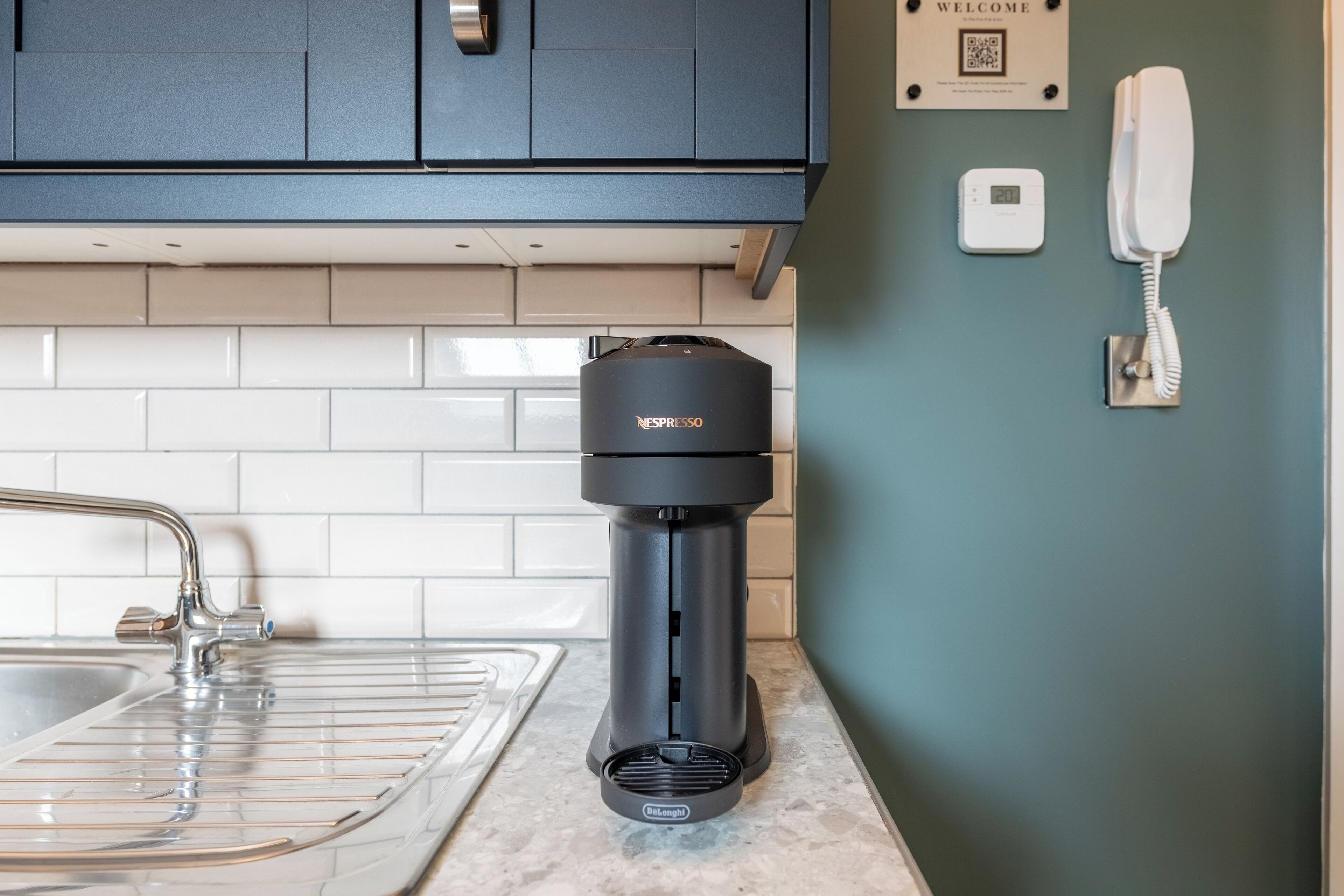 A kitchen with a coffee machine, a sink, and a wall-mounted phone.