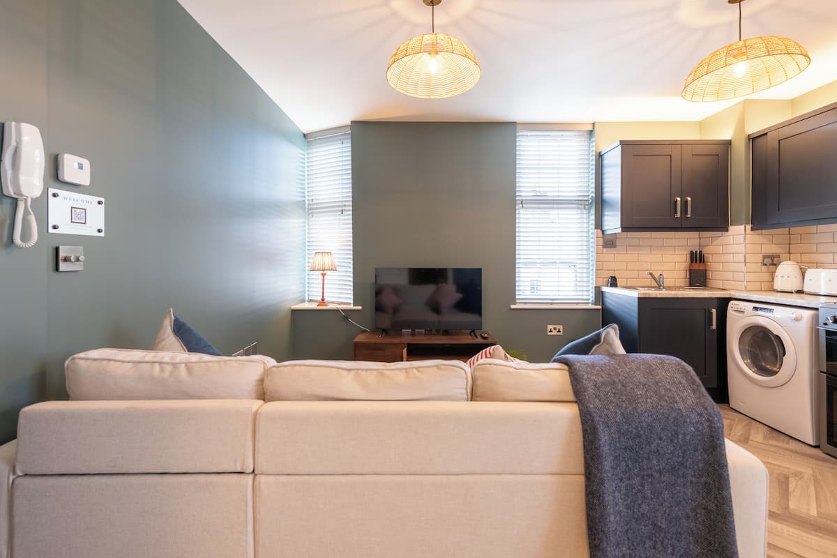 Una sala de estar moderna con sofá, televisor y una zona de cocina con armarios y lavadora.