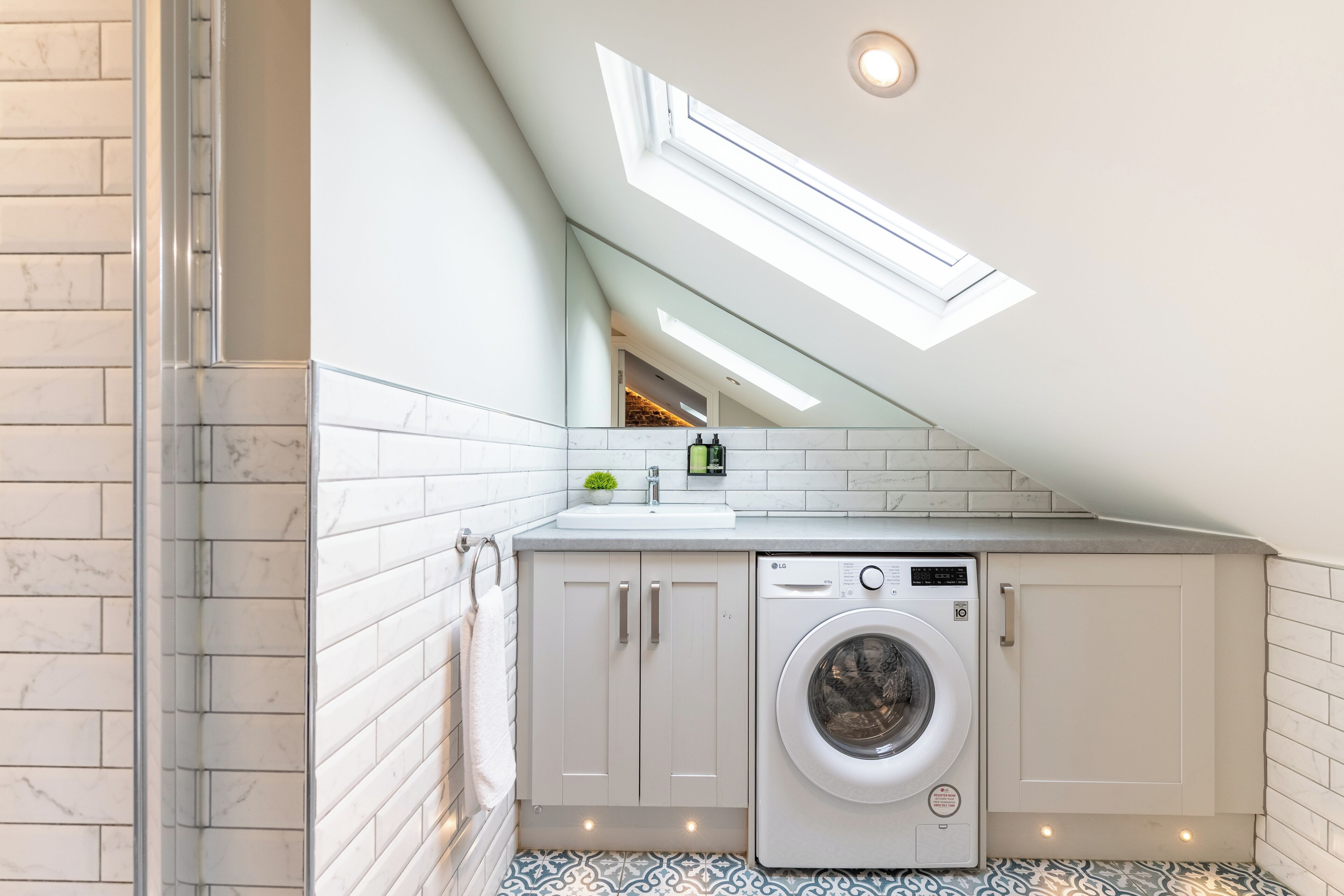 Une buanderie moderne avec un puits de lumière, des murs recouverts de carreaux blancs, un lave-linge et un évier.