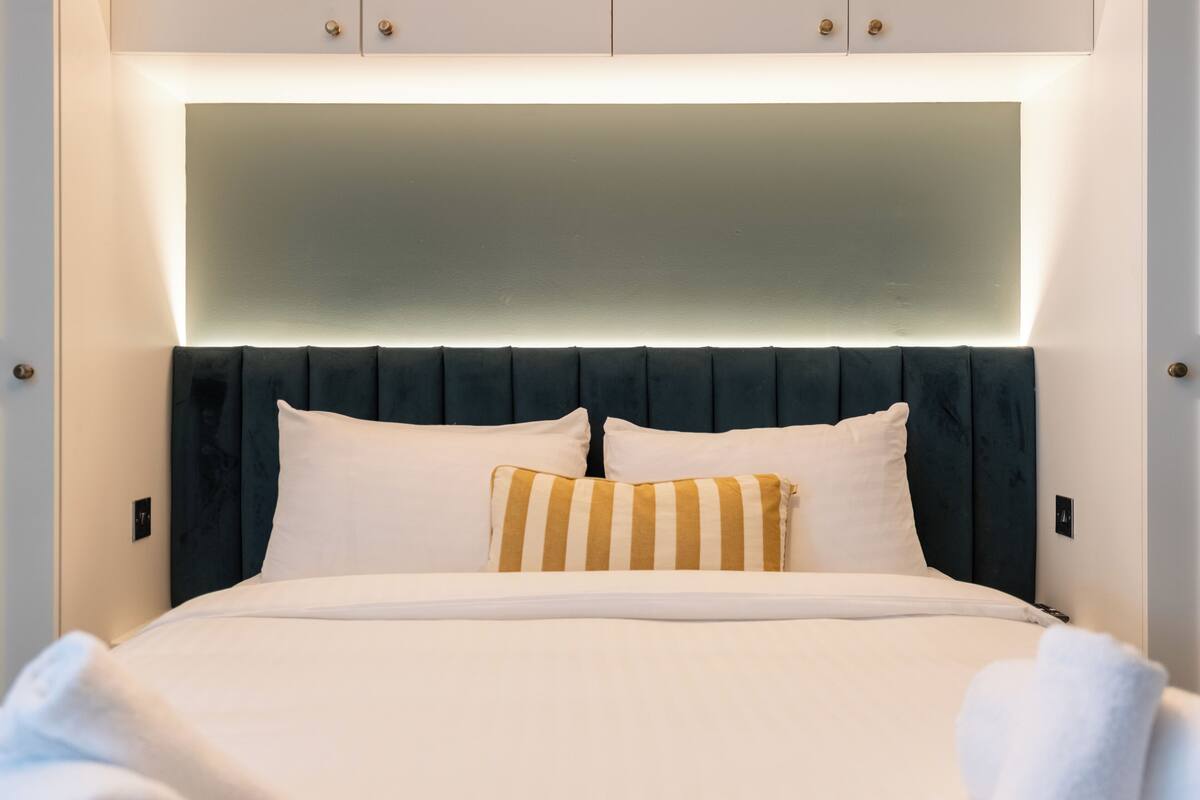 Una habitación de hotel moderna con una cama grande, cabecera oscura y pared de color claro.