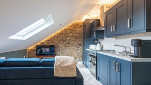 A modern kitchen with dark blue cabinets, a stone wall, and a skylight.