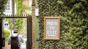 A man walking towards a gate with a sign that reads "PRESS TO EXIT."