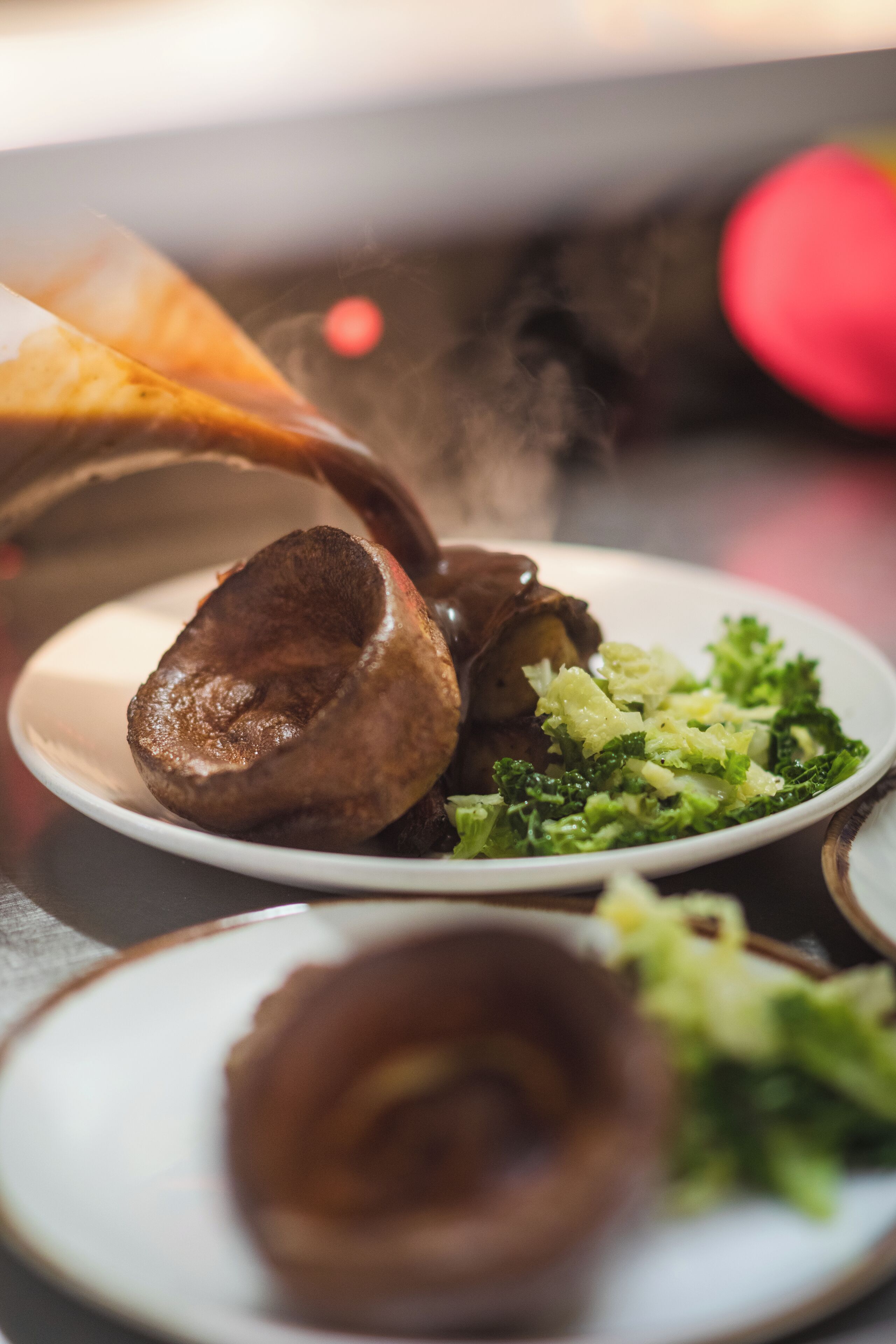 A plate with a Yorkshire pudding, broccoli, and a piece of meat, possibly beef, on a table.