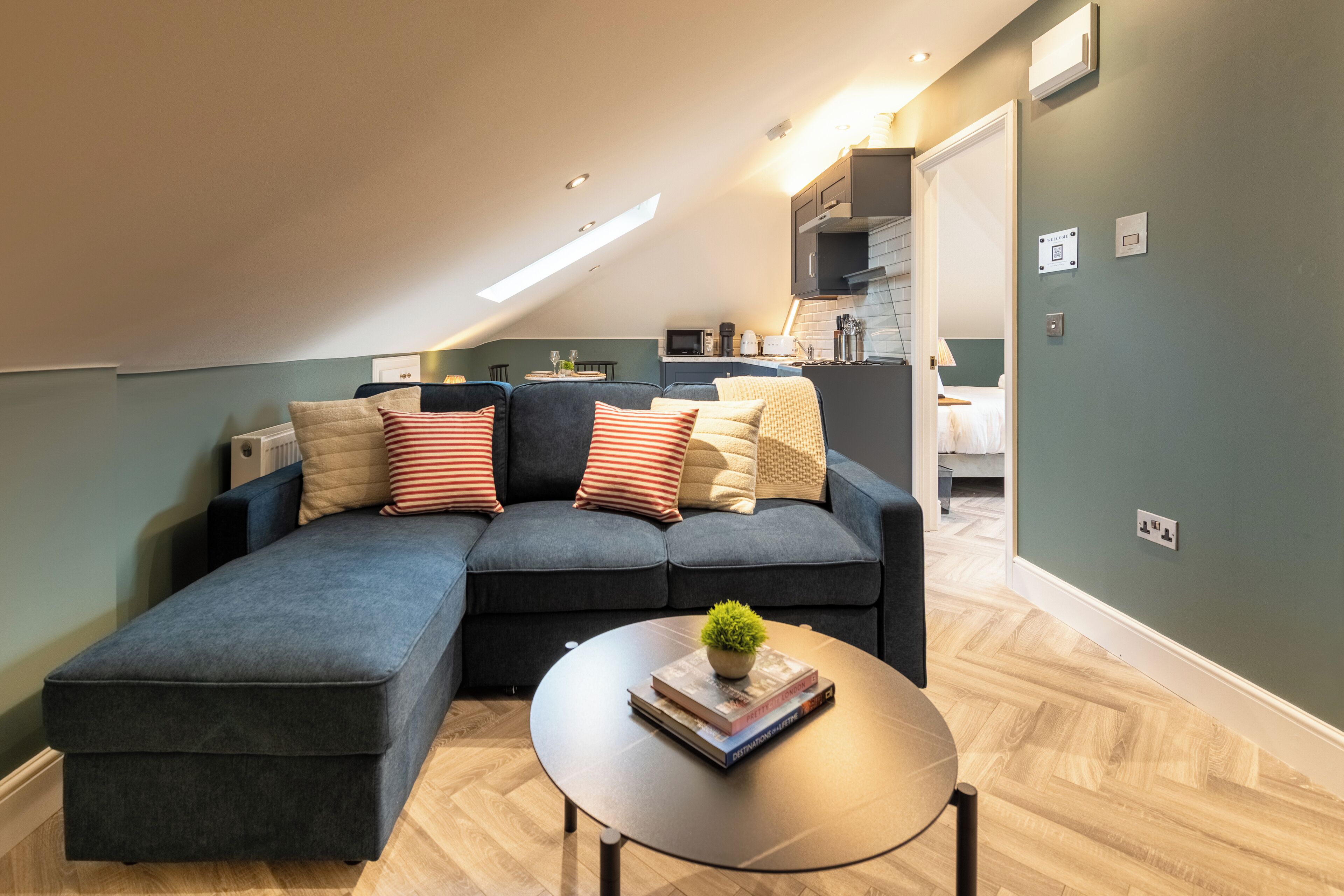 Een moderne woonkamer met een modulaire bank, een ronde salontafel met boeken en een plant, en een keuken op de achtergrond.