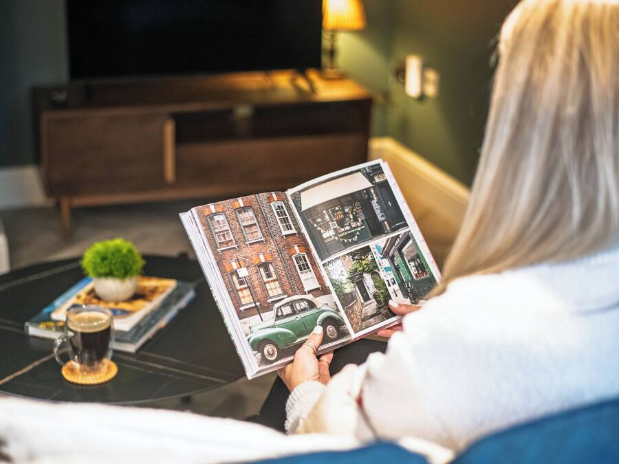 A person reading a magazine on a black coffee table with a small plant and a cup of coffee.