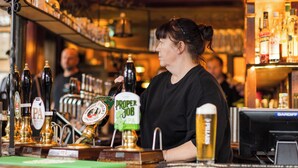 A bar with a wooden counter, various beer taps, and a person serving drinks.