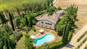 A villa with a swimming pool, surrounded by vineyards and tall trees.