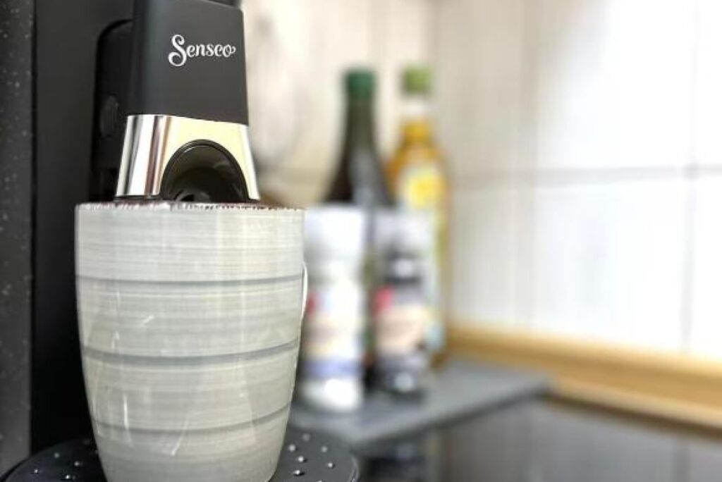 Una màquina de cafè Senseo servint cafè en un got de vidre transparent.
