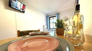 A dining area with a table set for two, a television mounted on the wall, and a window with curtains. - Apartment in Zwiesel Bavarian Forest, sauna, pool, Wi-Fi (Zwiesel)