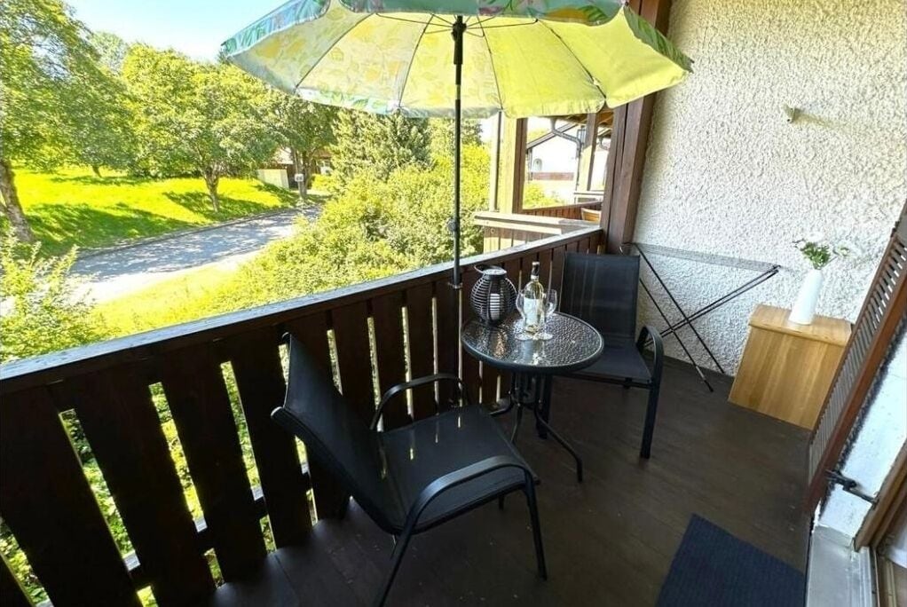 Un balcón con mesa, dos sillas, una sombrilla y vistas a un paisaje verde.