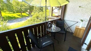 Un balcón con mesa, dos sillas, una sombrilla y vistas a un paisaje verde.