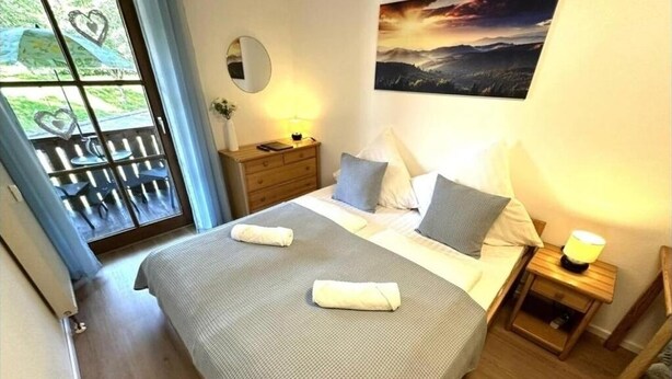A bedroom with a bed, bedside tables, a nightstand, a window with heart-shaped decorations, and a painting on the wall. - Apartment in Zwiesel Bavarian Forest, sauna, pool, Wi-Fi (Zwiesel)